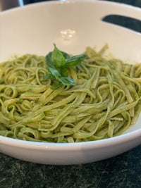 a white bowl of pasta with green pesto
